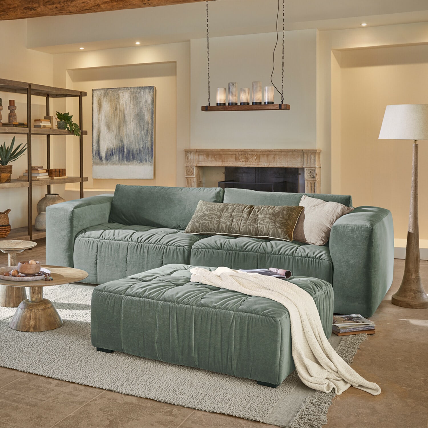 Canapé Ottolline Canapé vert en velours avec coussins et pouf dans un salon chaleureux avec cheminée et lampe sur pied