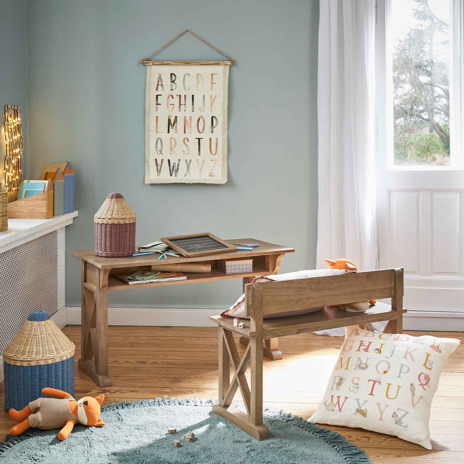 Houten bureau en bankje in kinderkamer met kussen en alfabetdecoratie aan de muur