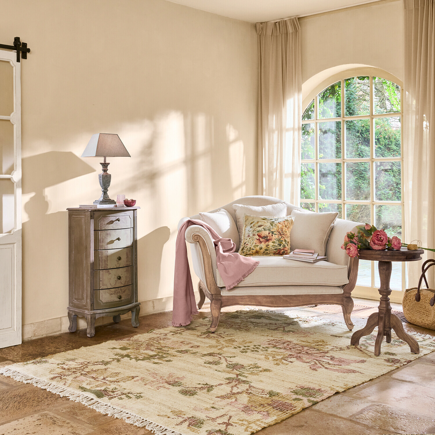 Gezellige woonkamer met beige houten bank, bloemenkussen en pastelkleuren vloerkleed bij groot raam