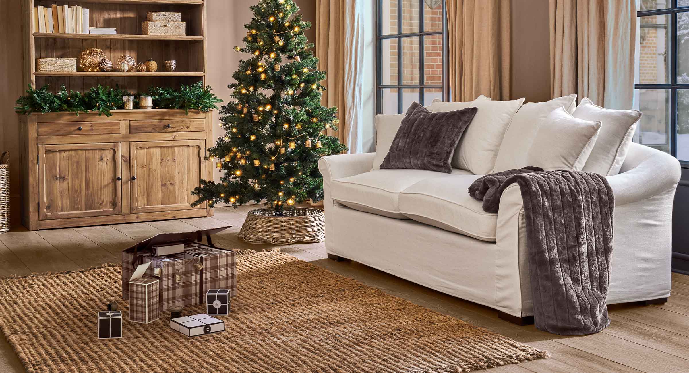 Gezellige woonkamer met witte bank, bruine kussens en verlichte kerstboom voor kerstdecoratie