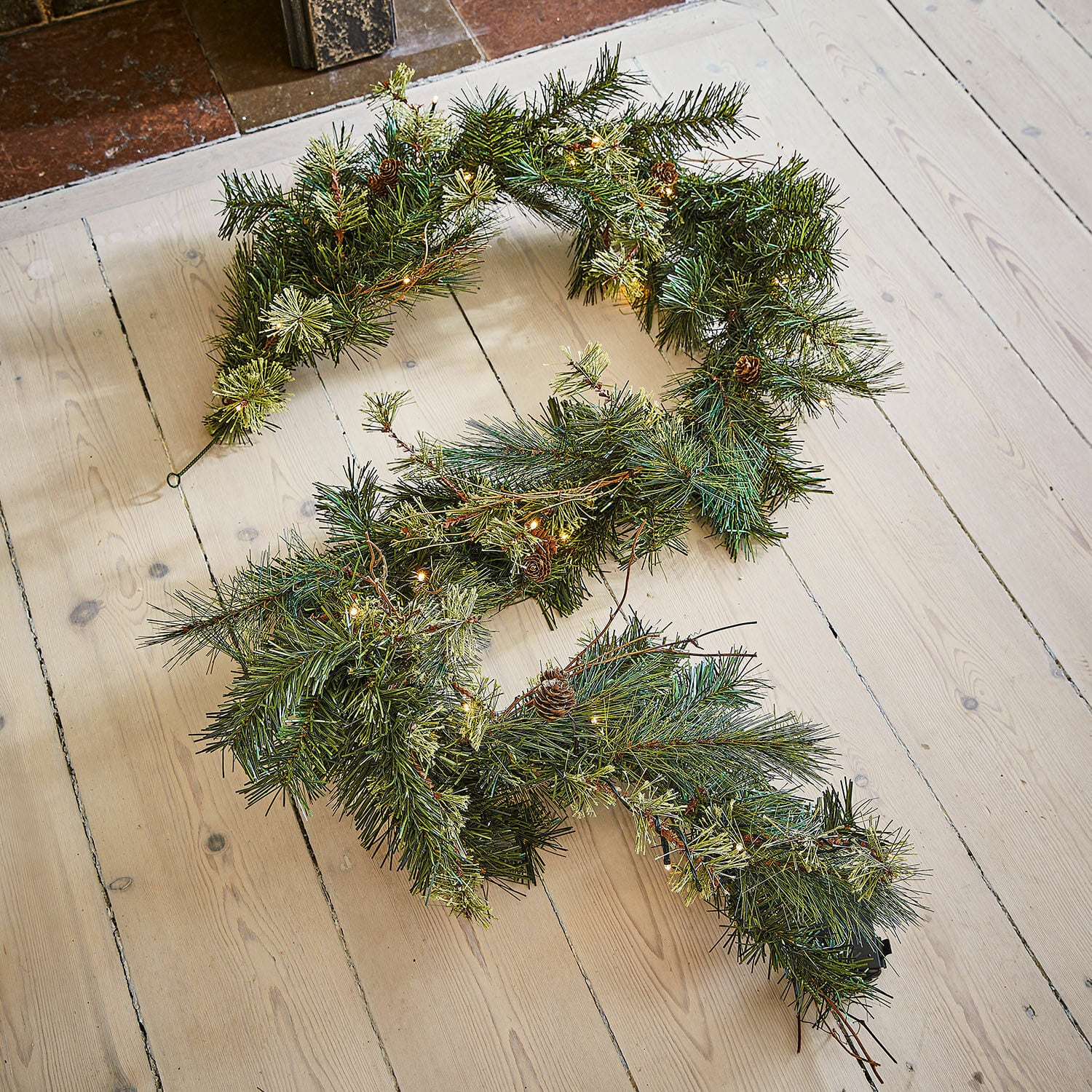Guirlande LED Enquilo Couronne de Noël verte avec aiguilles, petites pommes de pin et lumières LED décoratives sur plancher clair