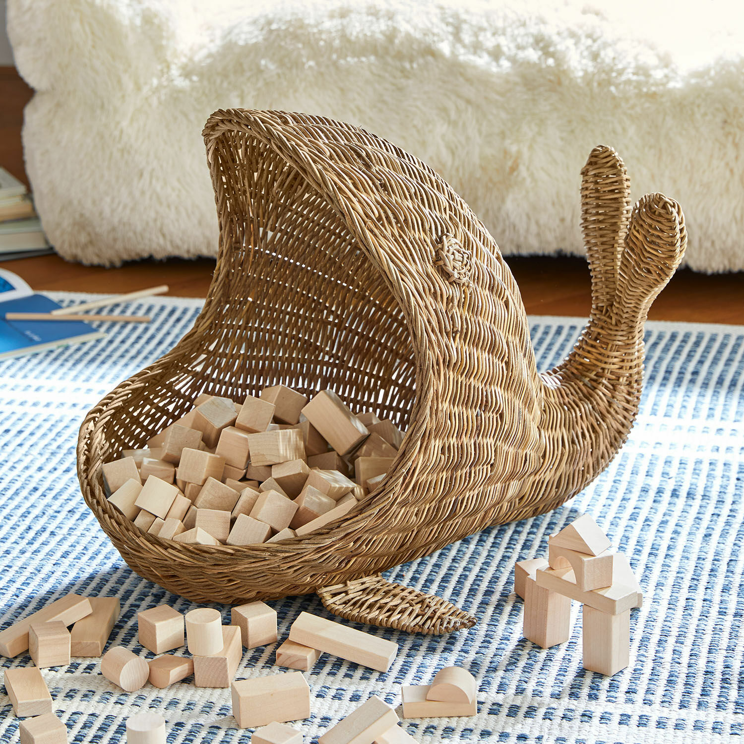 Mand Cheruboo Mand in walvisvorm van natuurlijk riet met houten blokken op een blauw patroon tapijt
