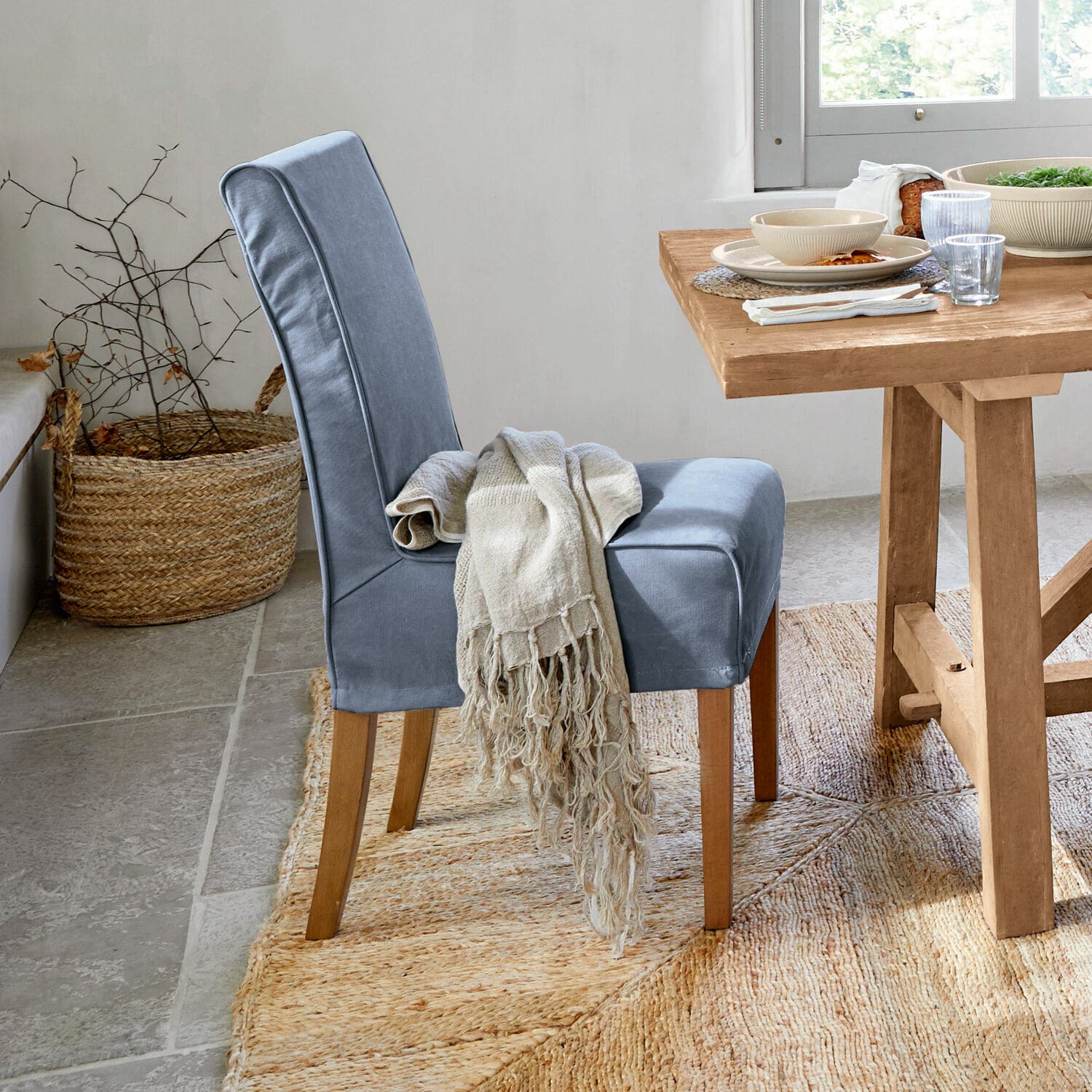 Chaise bleue rembourrée avec pieds en bois et plaid beige près d'une table en bois clair