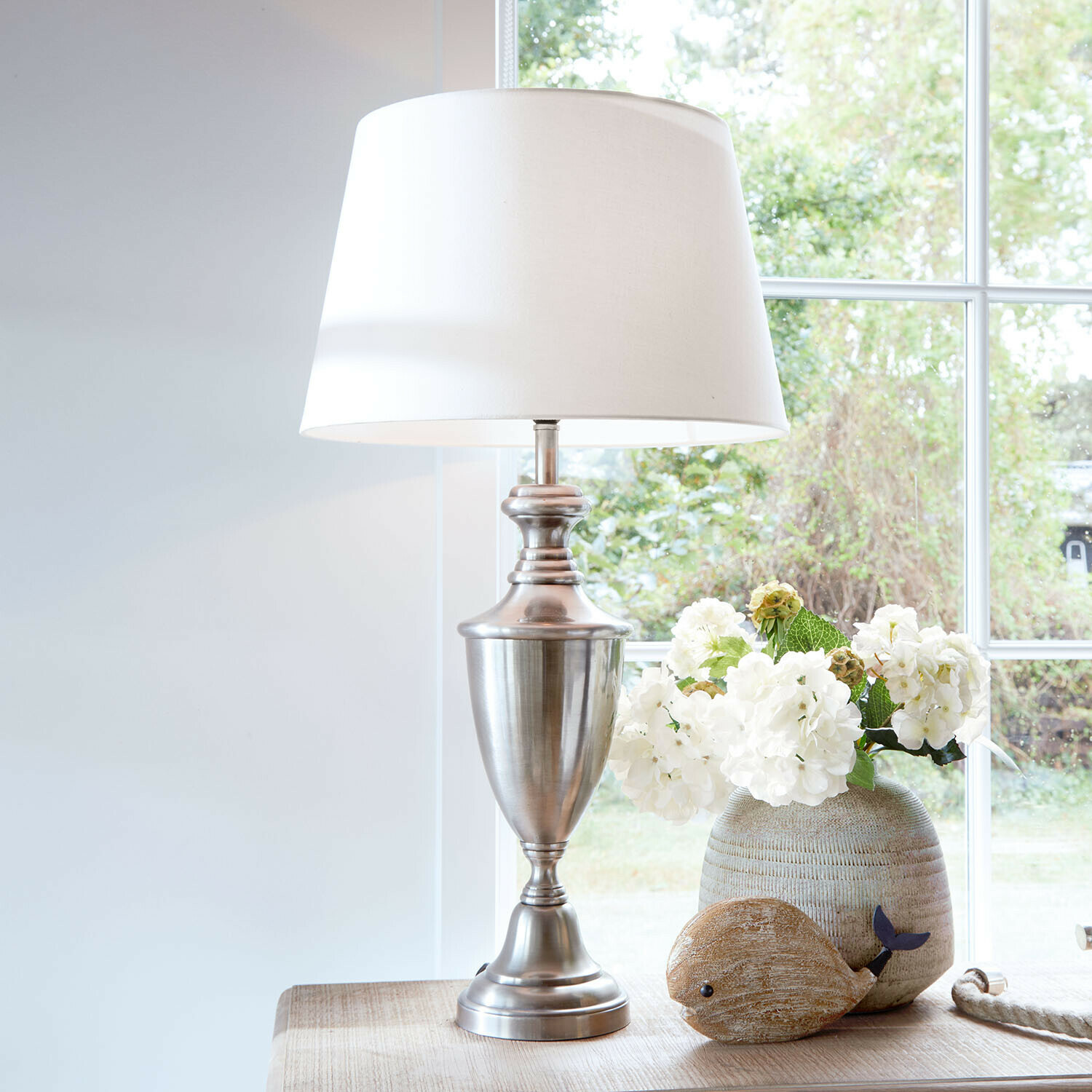 Tafellamp Montalure Tafellamp met metalen voet en witte kap op houten tafel met bloemendecoratie