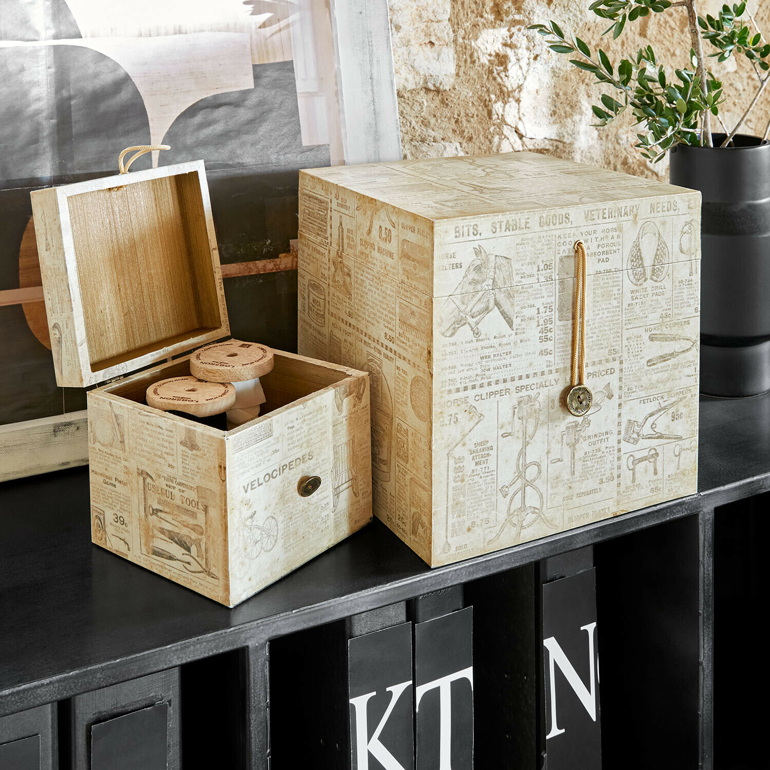 Boîtes décoratives en bois beige avec imprimé vintage posées sur une étagère noire pour rangement