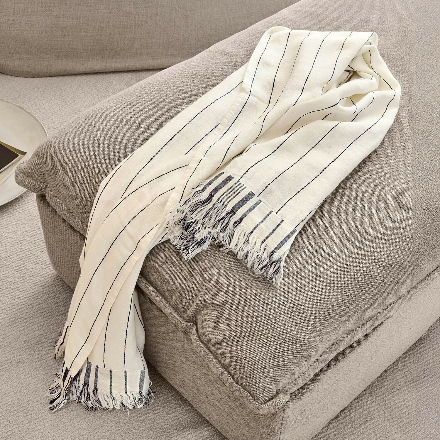 Plaid Ulderina Plaid beige en coton avec rayures noires et franges sur fauteuil gris, décoration intérieure cosy