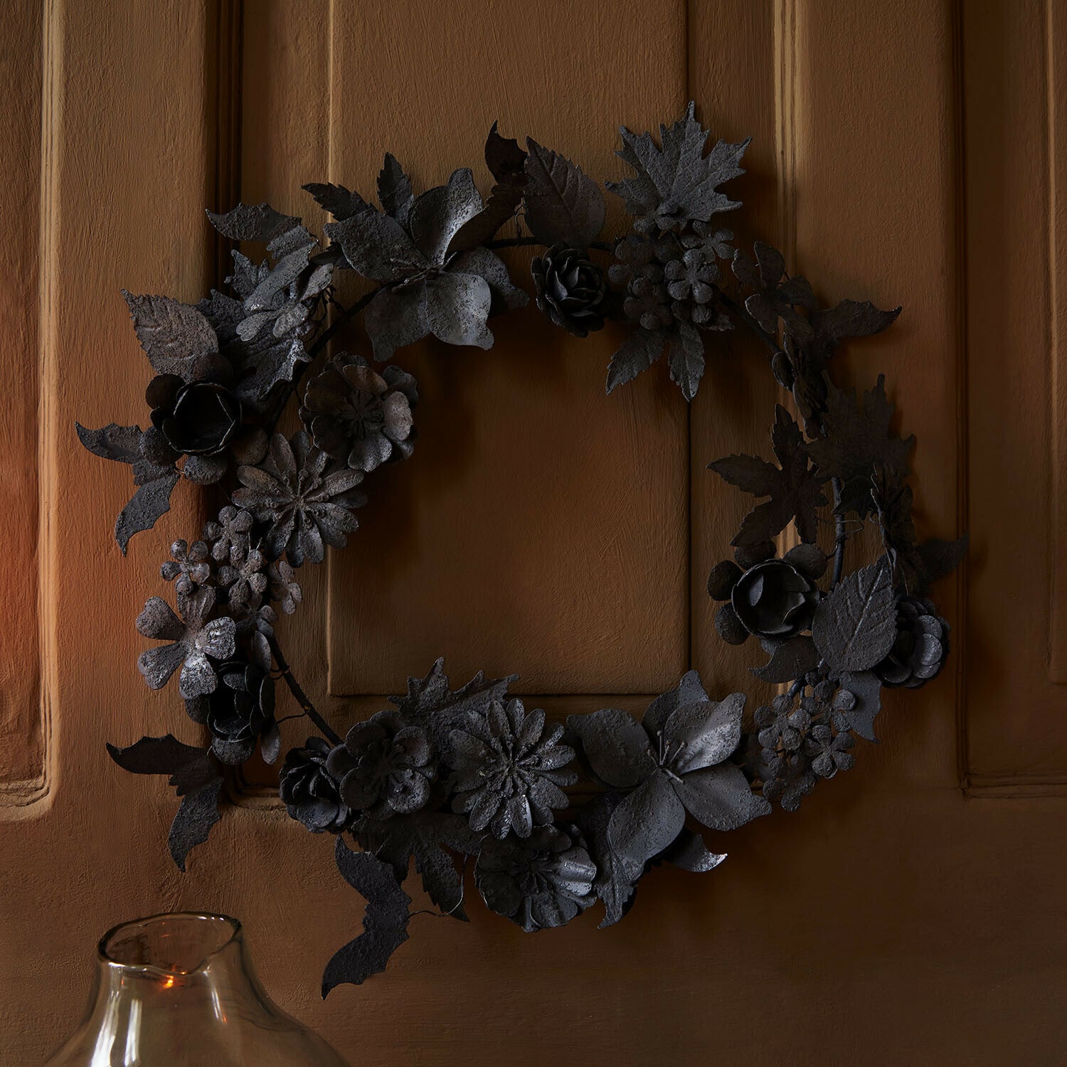 Couronne décorative en métal noir avec feuilles et fleurs sur une porte marron pour décoration intérieure