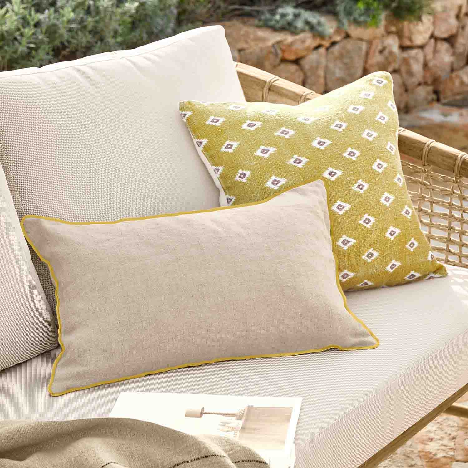 Coussin beige avec bordure jaune et coussin jaune à motifs blancs sur canapé en rotin extérieur