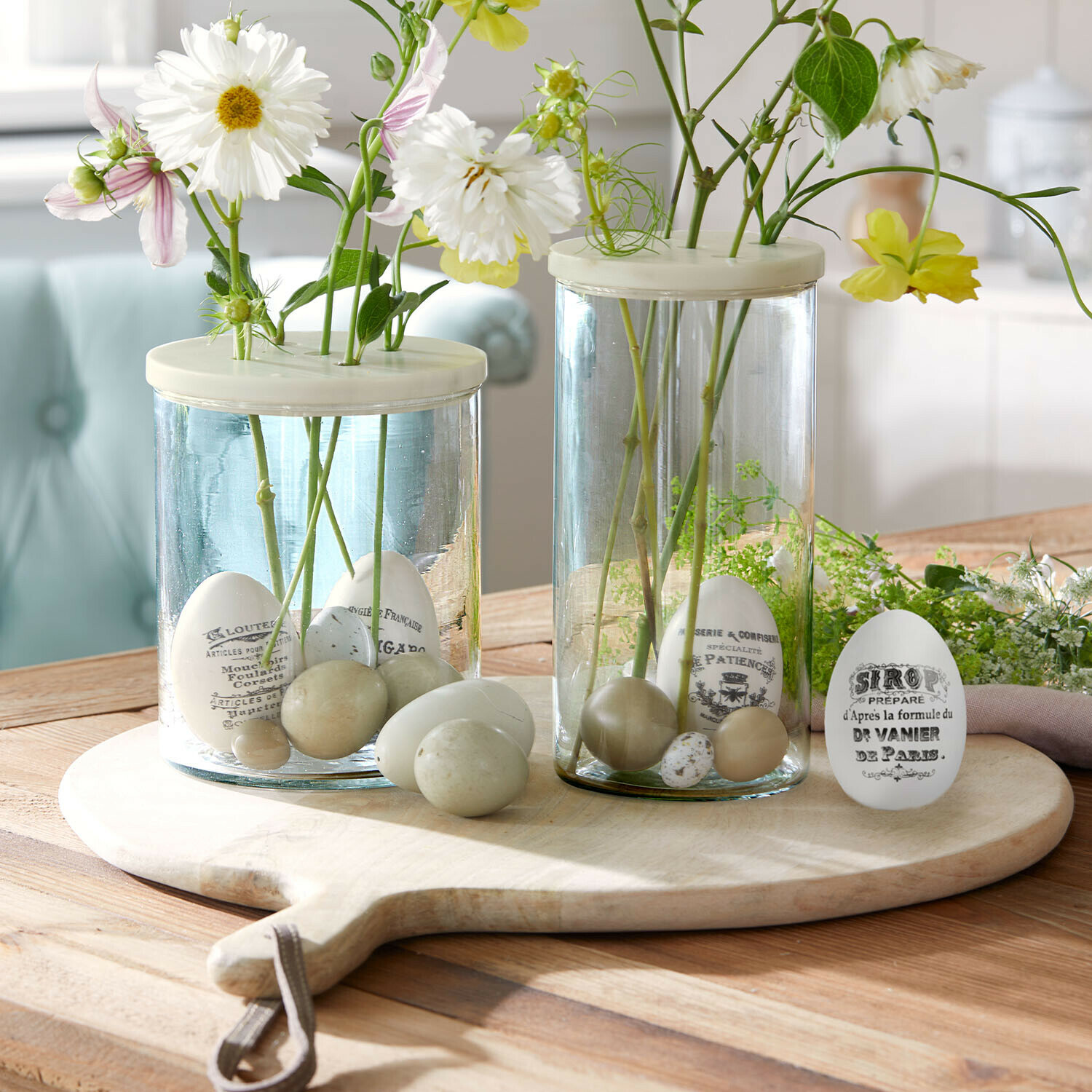 Paasei set van 4 Maison Vélour Glazen vazen met witte en beige decoratieve eieren en bloemen op een houten snijplank