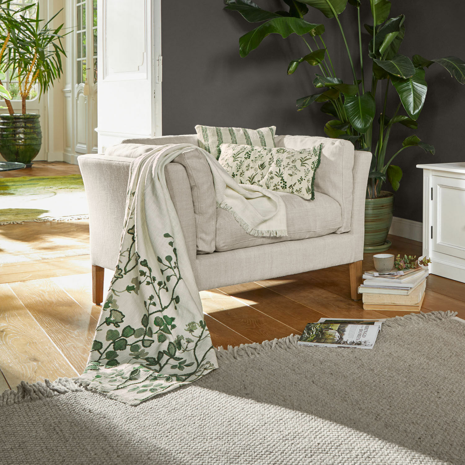 Fauteuil Lourvière Beige stoffen bank met groene kussens en decoratief deken met plantenmotief in woonkamer