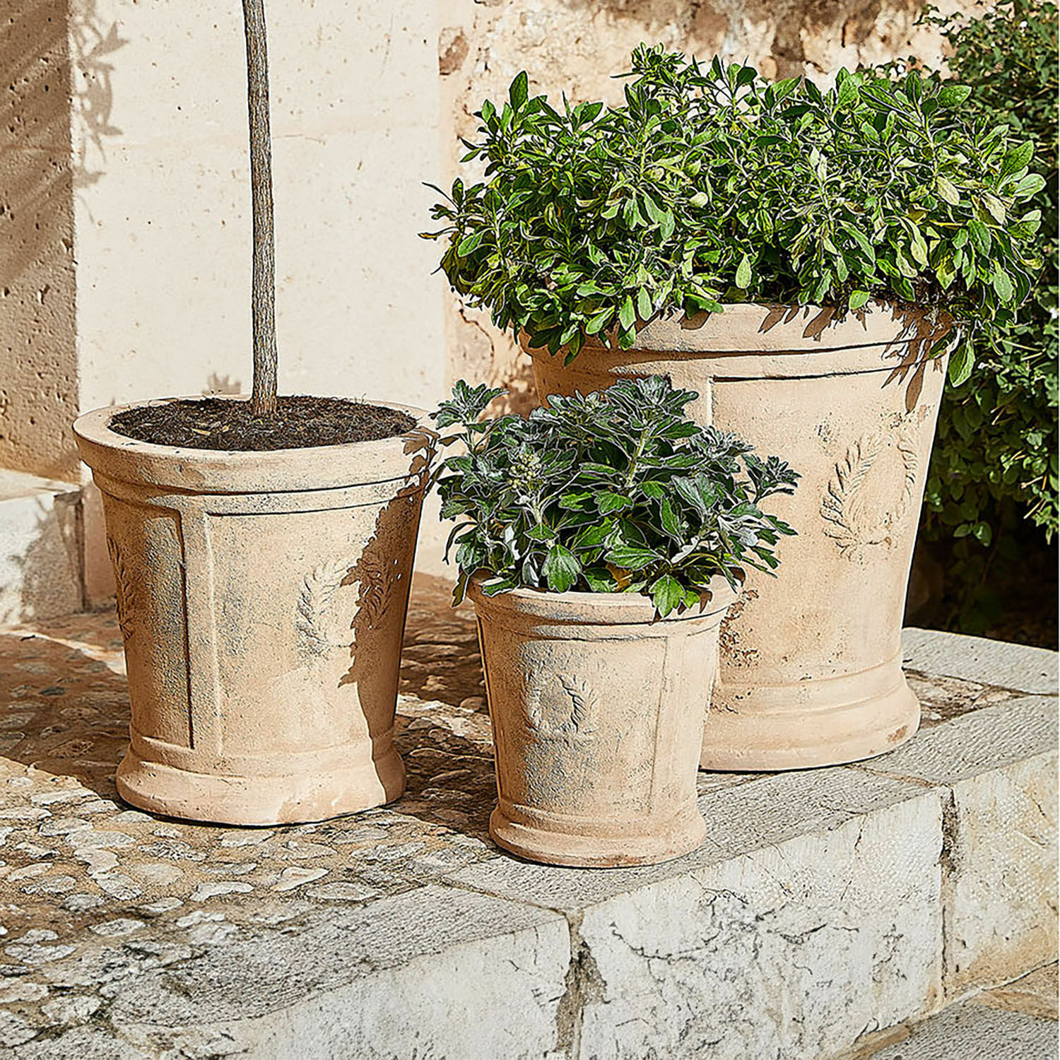 Sierpot set van 3 Nesrin Drie beige terracotta bloempotten met planten op stenen terras, decoratieve tuinpotten