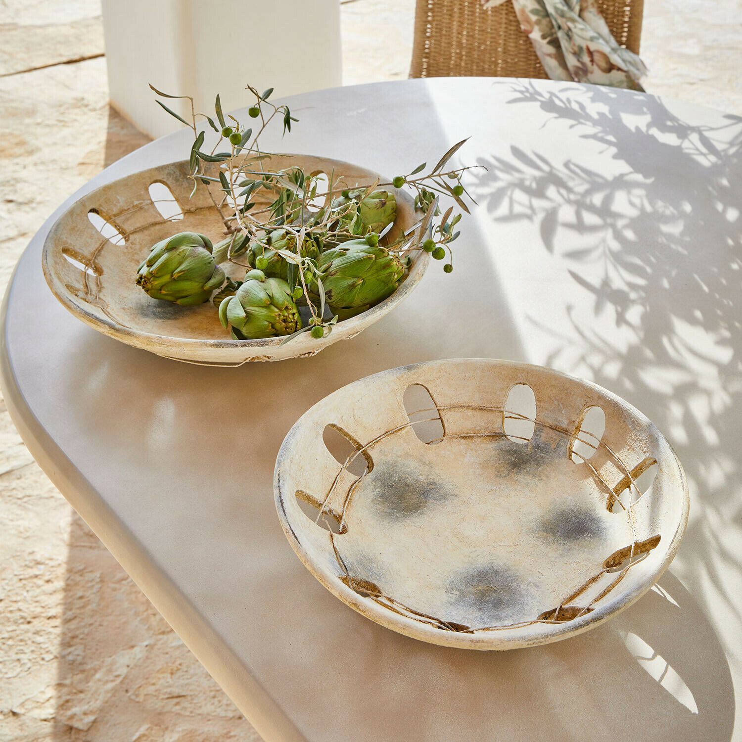 Deux bols décoratifs en céramique beige sur une table, l'un contenant des artichauts verts