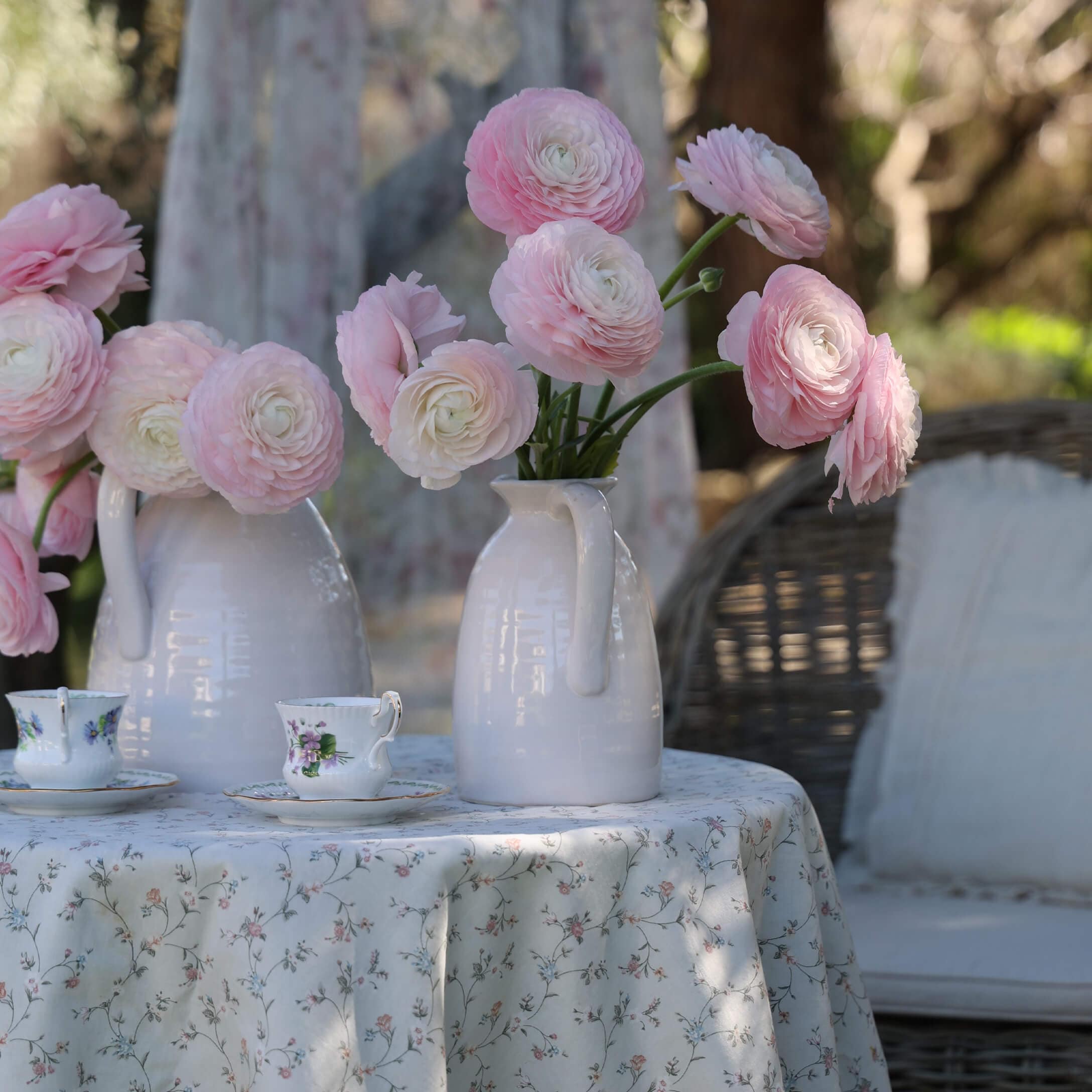 Carafes en céramique blanche avec fleurs roses sur une table à nappe fleurie et tasses à thé décoratives