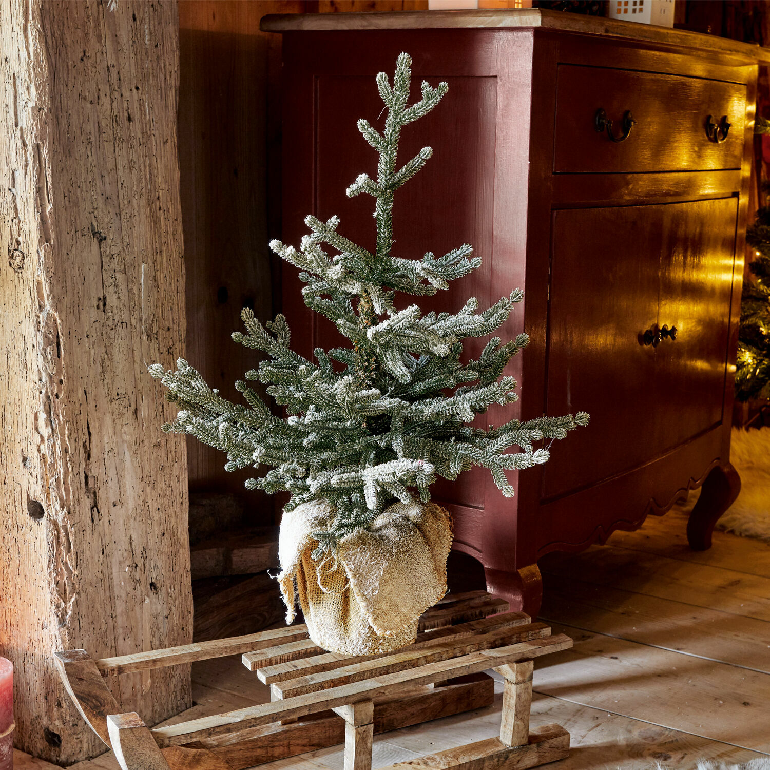 Sierboom Glenda Kleine kunstmatige besneeuwde kerstboom op houten slee in rustieke warme kamer