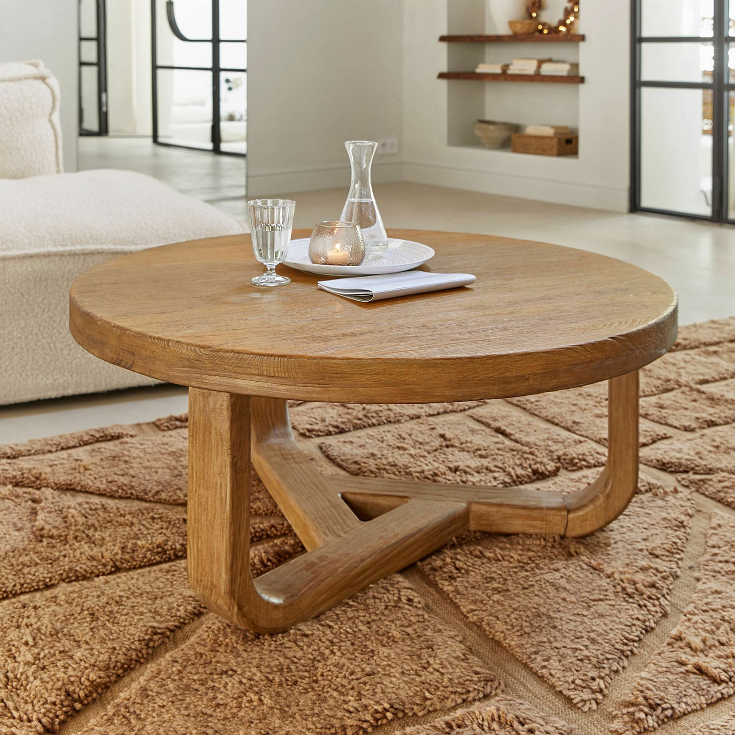 Salontafel Trésorique Ronde salontafel van natuurlijk eikenhout op een zachte bruine vloerkleed in een woonkamer