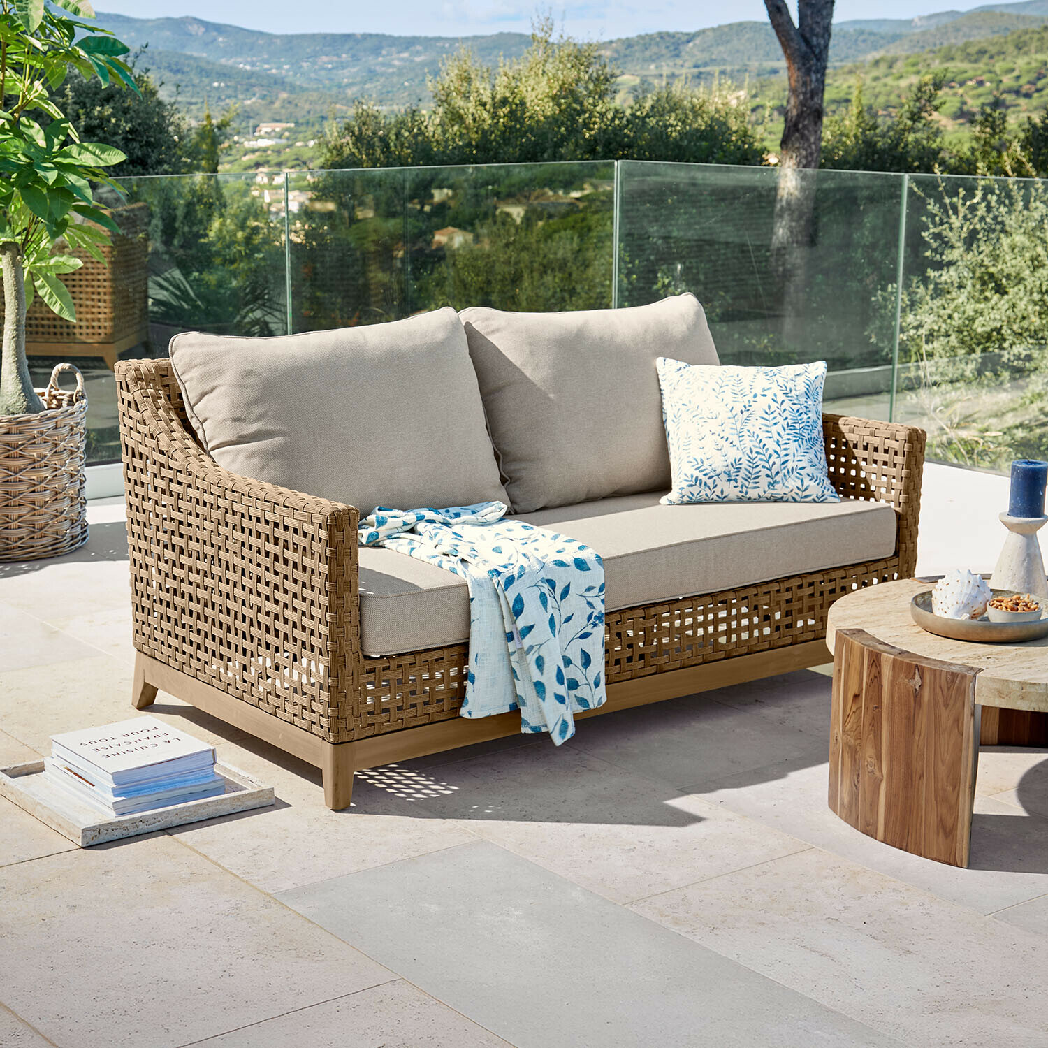 Bank Isolara Buitensofa van natuurlijk gevlochten riet met beige kussens en blauw bladmotief deken