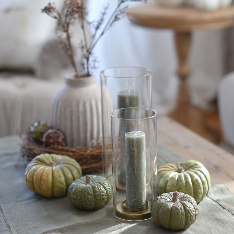 Decoratieve groene kaarsen en pompoenen in glazen windlichten op houten tafel in natuurlijke stijl