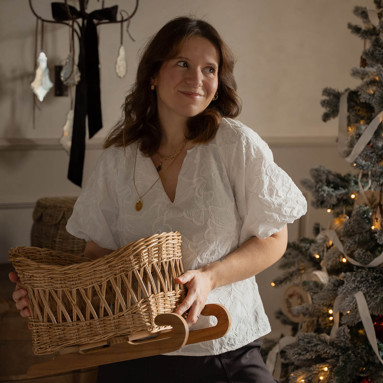 Femme en blouse blanche tenant un traîneau en osier avec base en bois près d'un sapin décoré