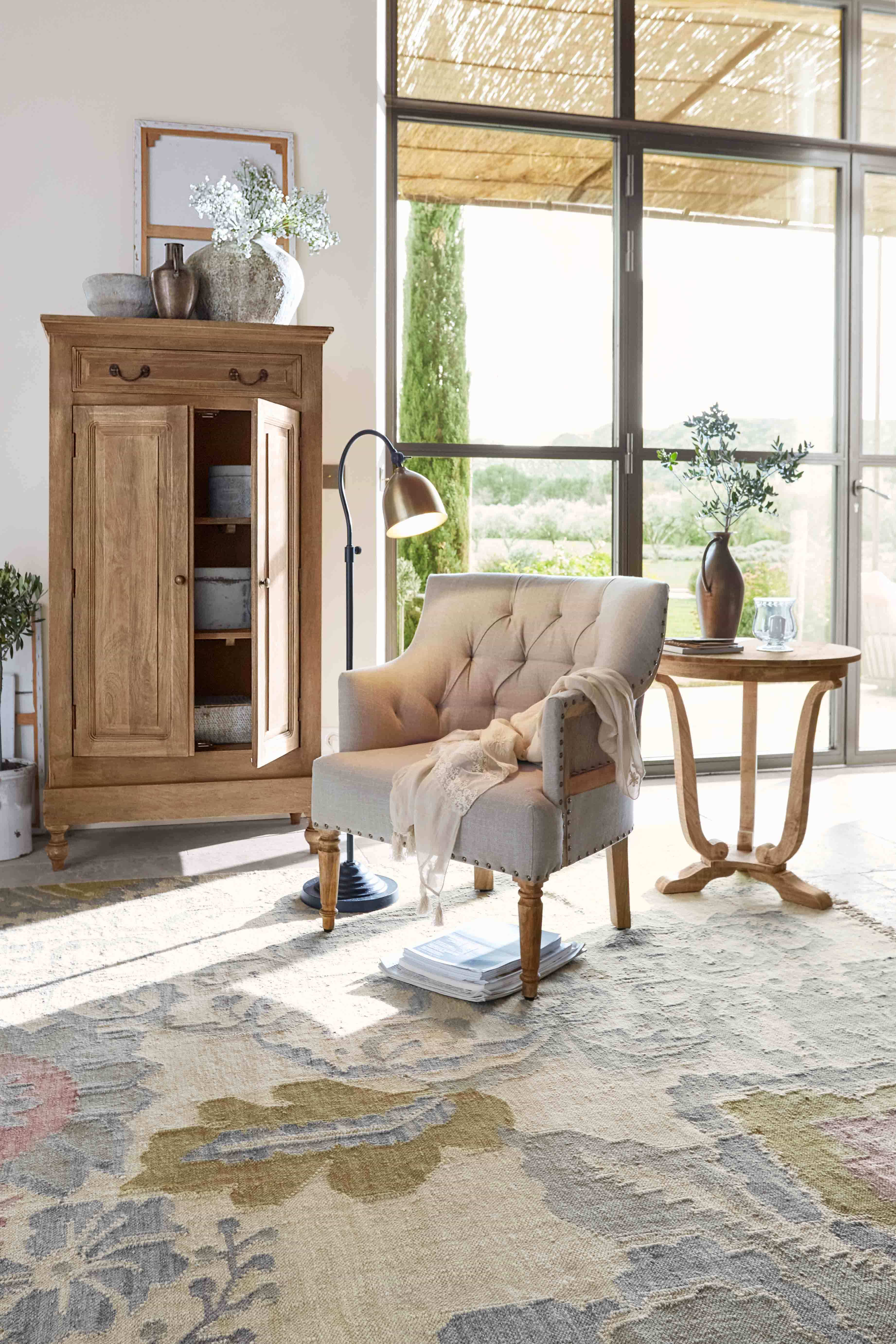 Fauteuil beige avec pieds en bois et table d'appoint en bois dans un salon lumineux avec grande fenêtre