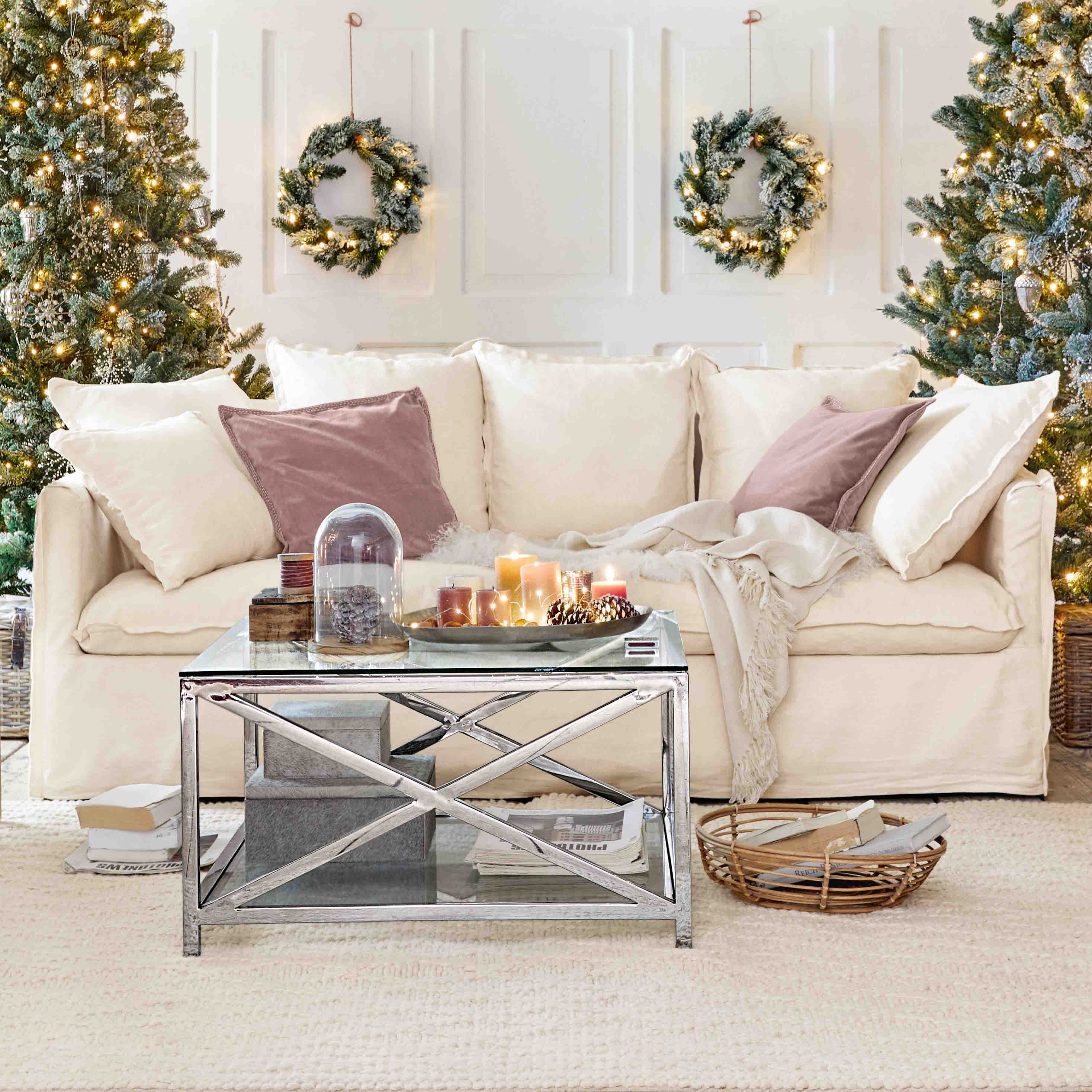 Canapé crème confortable avec coussins et table basse en métal dans un décor de Noël avec sapins et couronnes