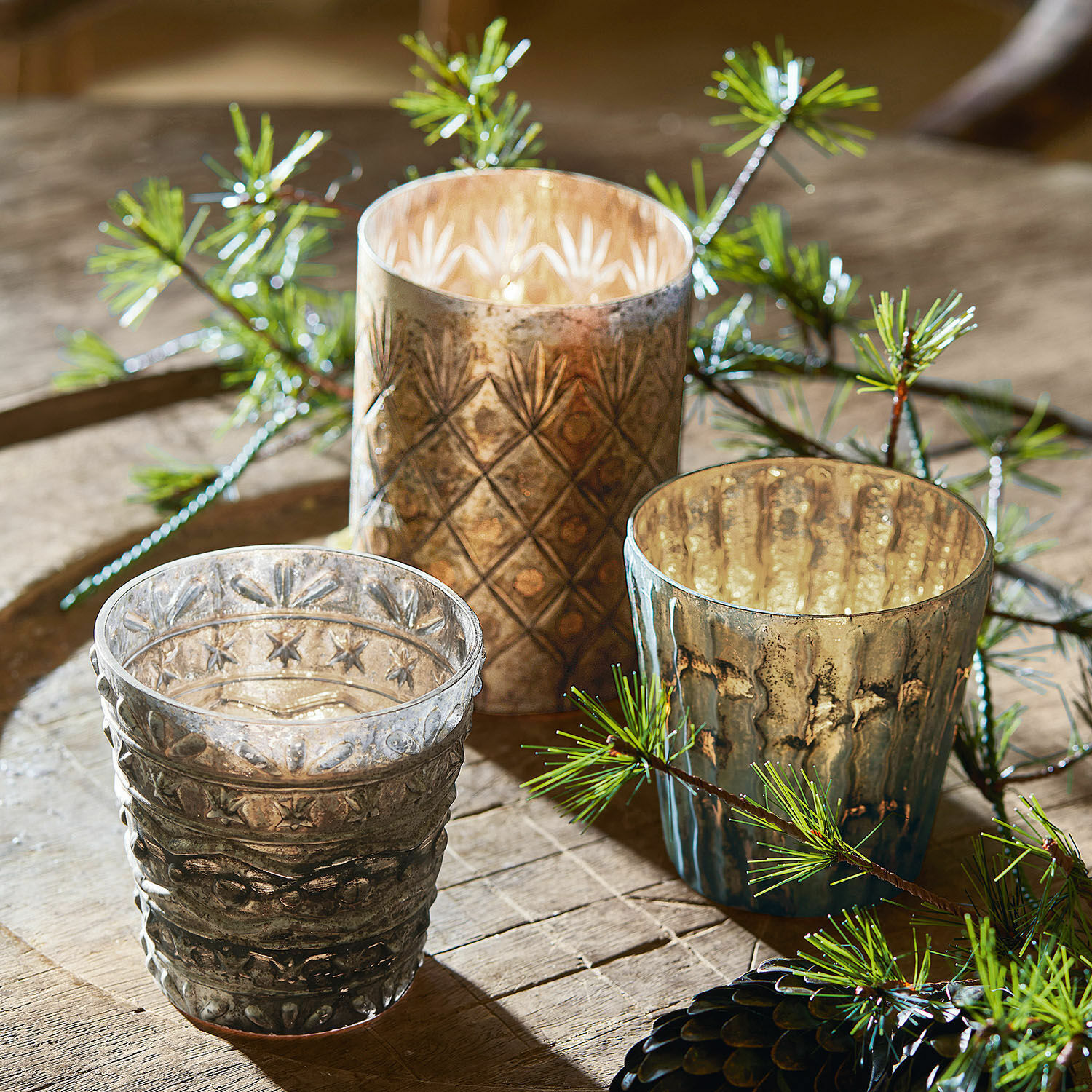 Ensemble de trois photophores en verre avec motifs décoratifs en tons bruns et gris sur une table en bois
