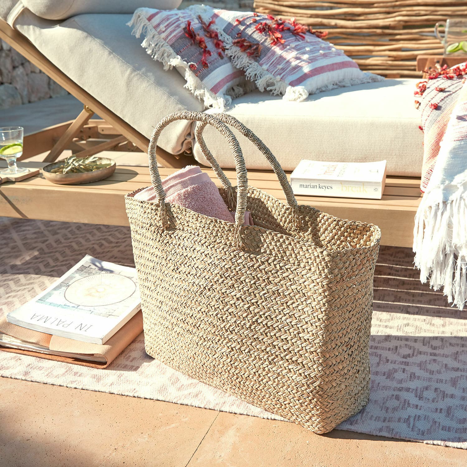 Cabas Ventresque Sac tressé naturel en herbe marine avec serviette rose sur terrasse près d'une chaise longue