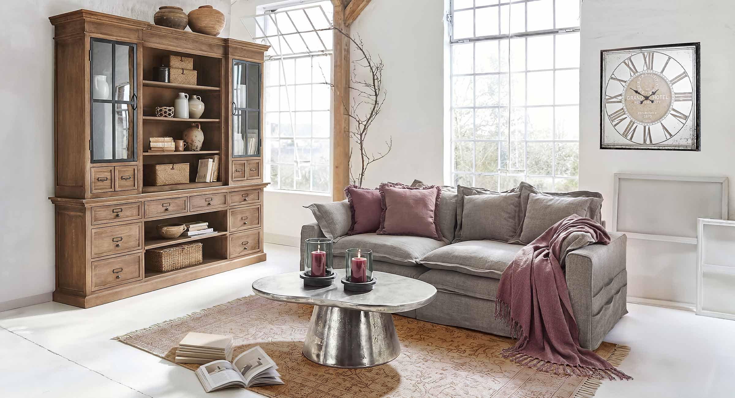 Gezellige woonkamer met grijze bank, bordeauxrode kussens en houten vitrinekast in vintage stijl