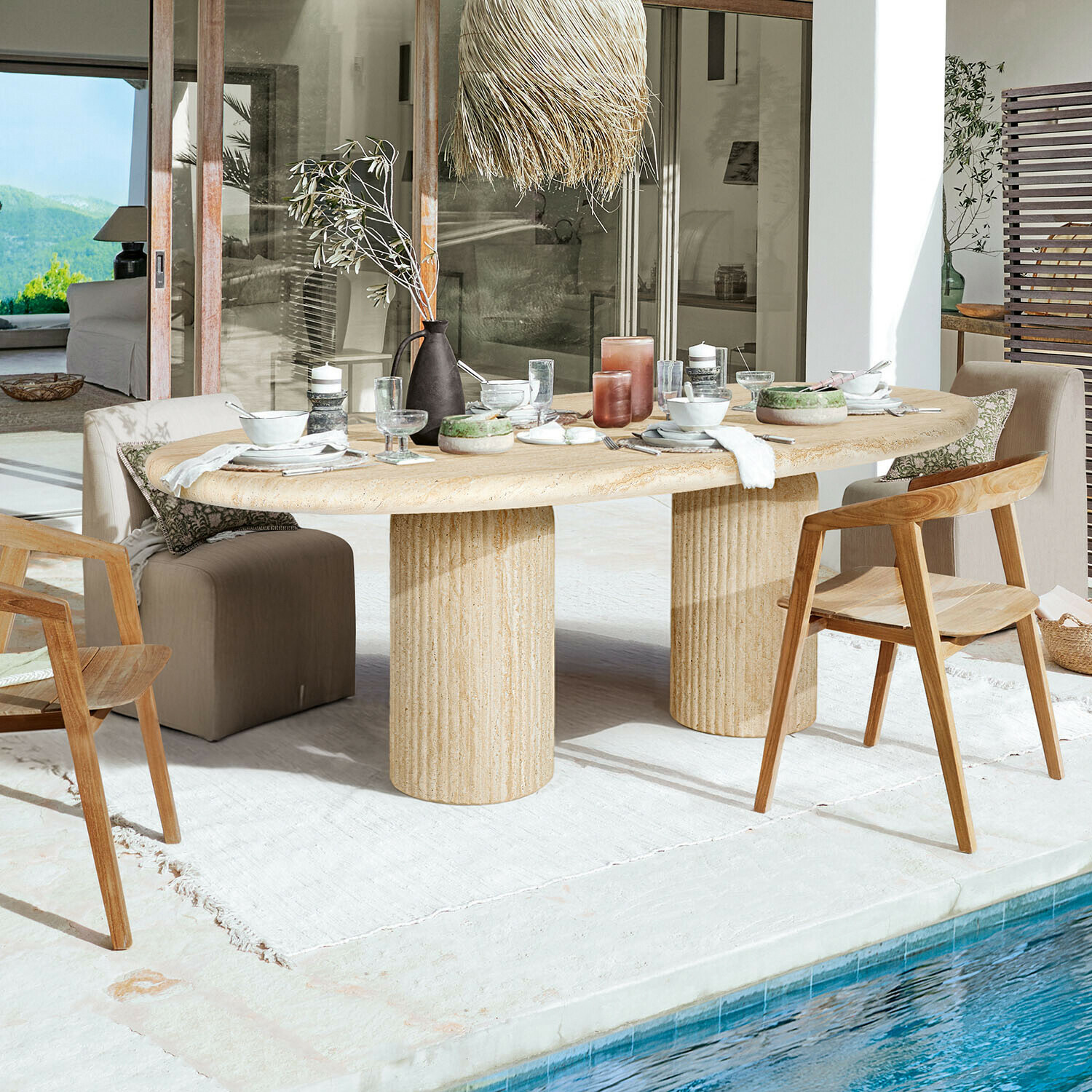 Table Calerio Table ovale en pierre beige avec deux pieds cylindriques sur terrasse au bord de la piscine avec chaises en bois