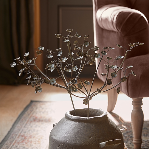 Branche décorative en métal avec fleurs dans un vase en céramique grise près d'un fauteuil rose