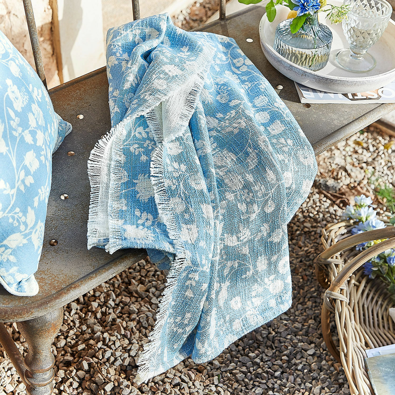 Plaid Corvelique Blauwe katoenen deken met wit bloemenpatroon op metalen bank in de tuin