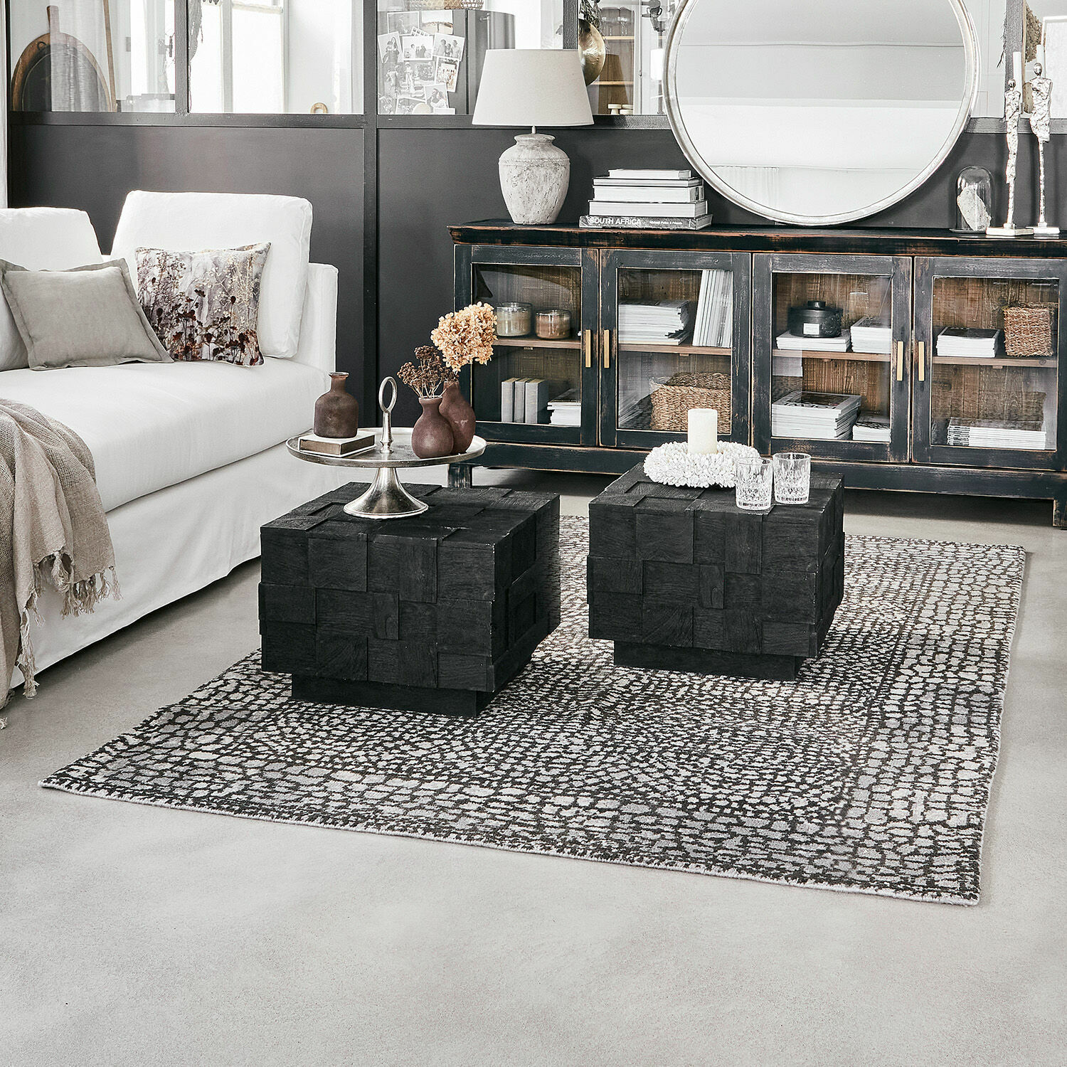 Vloerkleed Vermont Twee zwarte houten salontafels op een patroon vloerkleed in een moderne woonkamer met witte bank
