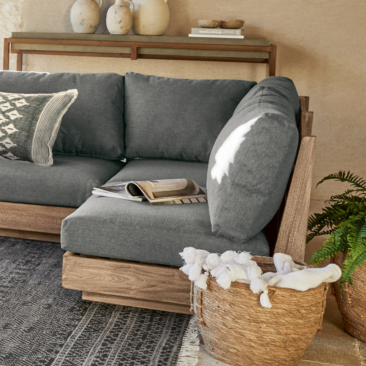 Zitelement Courtelevant Grijze bank met houten frame en zachte kussens in moderne woonkamer met rieten mand