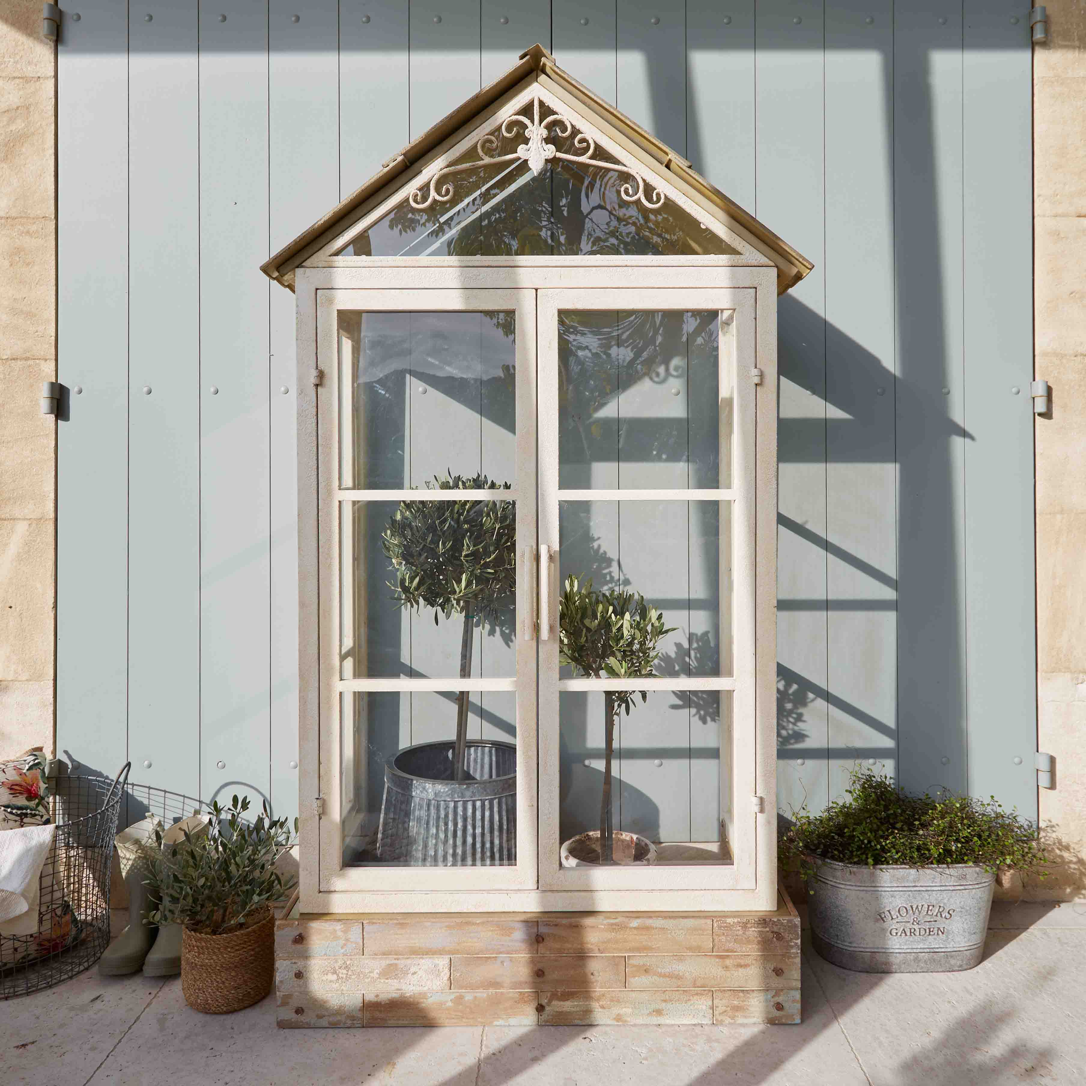 Witte houten kas met decoratief dak en planten in potten op zonnig terras