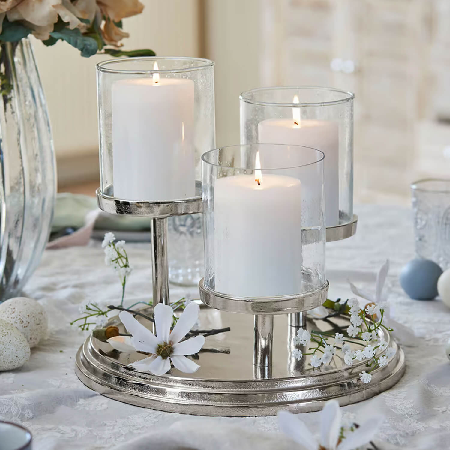 Bougeoir triple en métal argenté avec trois bougies blanches et fleurs décoratives sur une table