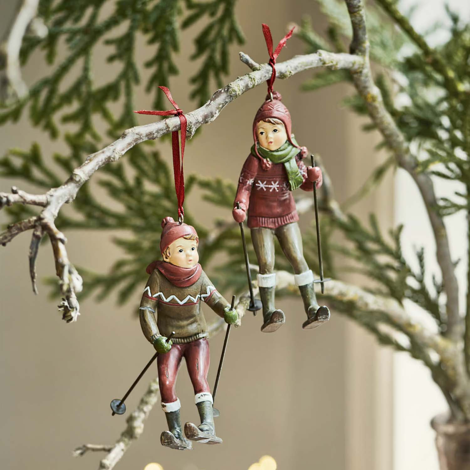 Deux décorations suspendues représentant des enfants en tenue de ski rouge et verte sur une branche