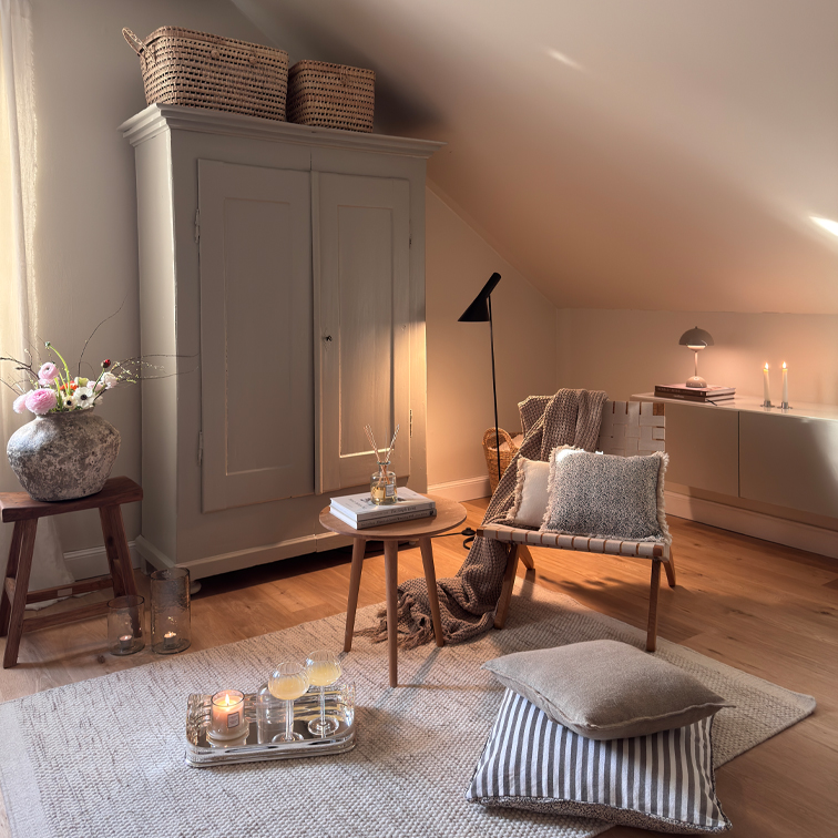 Salon chaleureux avec fauteuil beige, table en bois et armoire sous pente, décorations et lampes