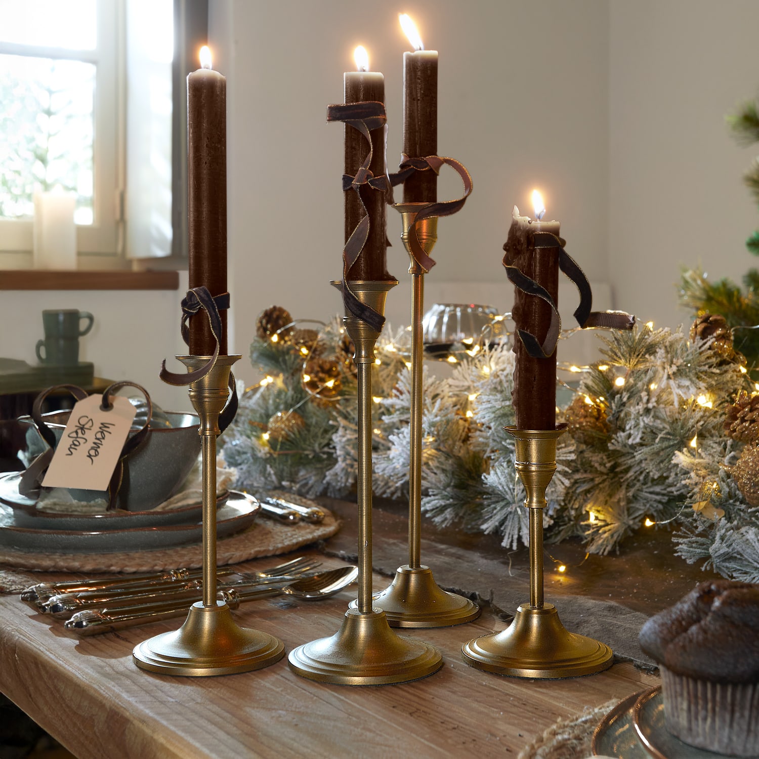 Set van vier gouden kandelaars met bruine kaarsen en decoratieve linten op een houten tafel