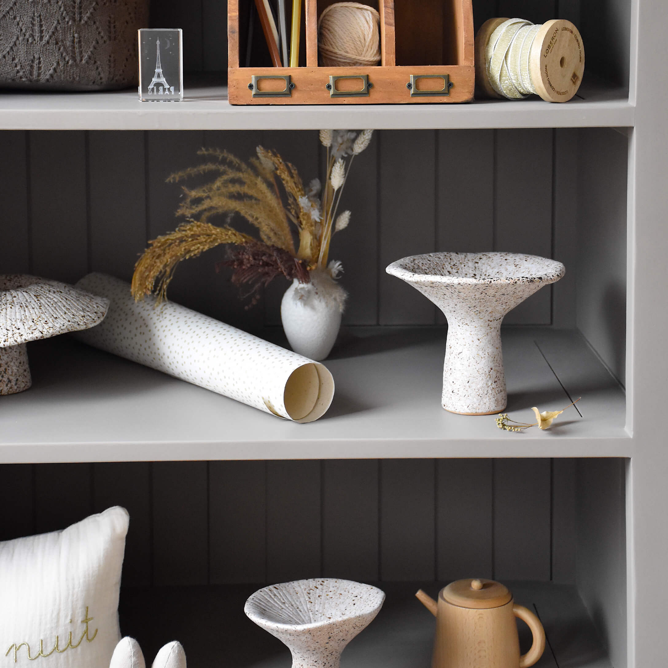 Bol en céramique blanche tachetée de brun sur étagère grise avec décorations et fleurs séchées