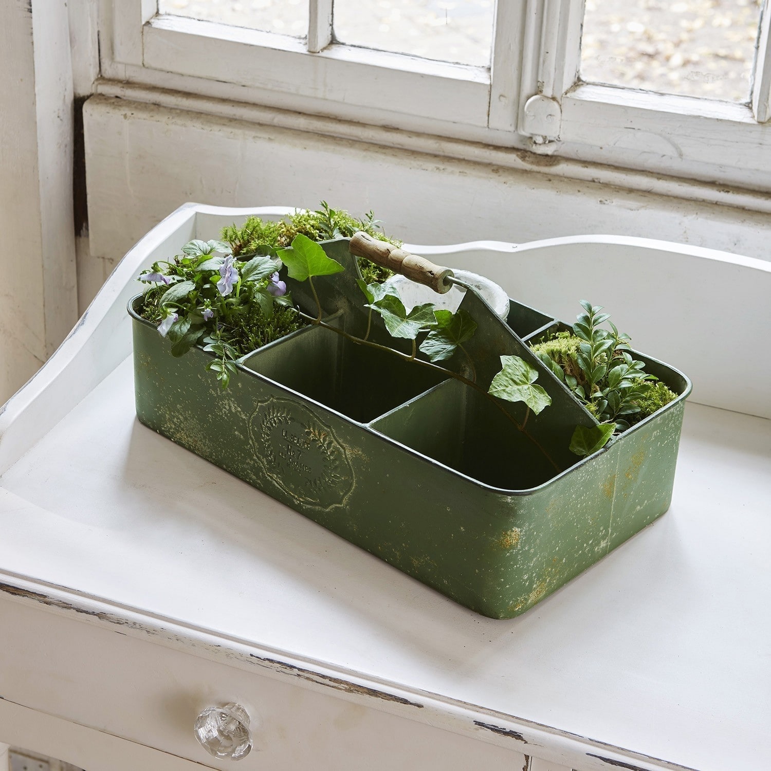 Groene metalen doos met vakken en houten handvat, versierd met planten en mos
