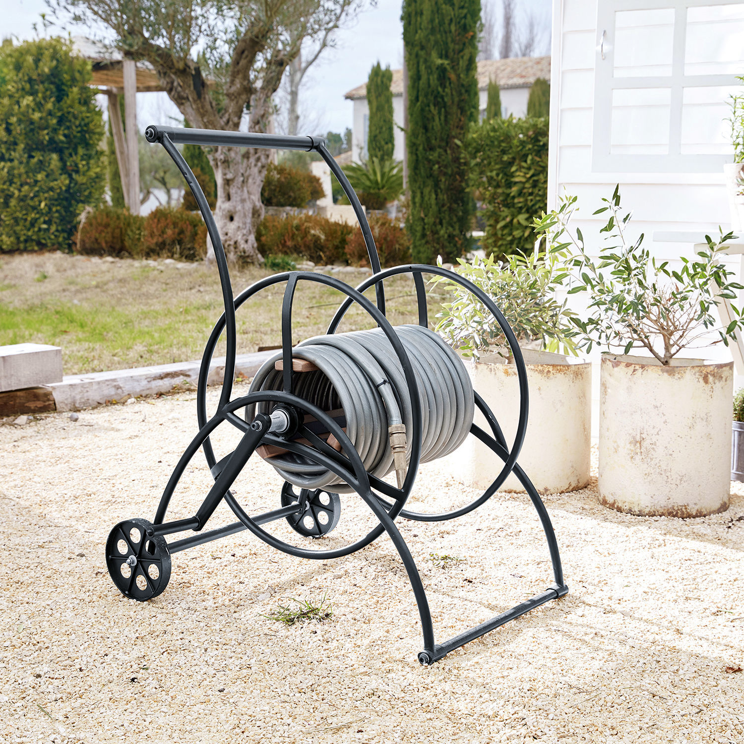 Chariot enrouleur de tuyau d’arrosage Middleby Chariot en métal noir avec tuyau d'arrosage gris sur sol gravillonné dans un jardin