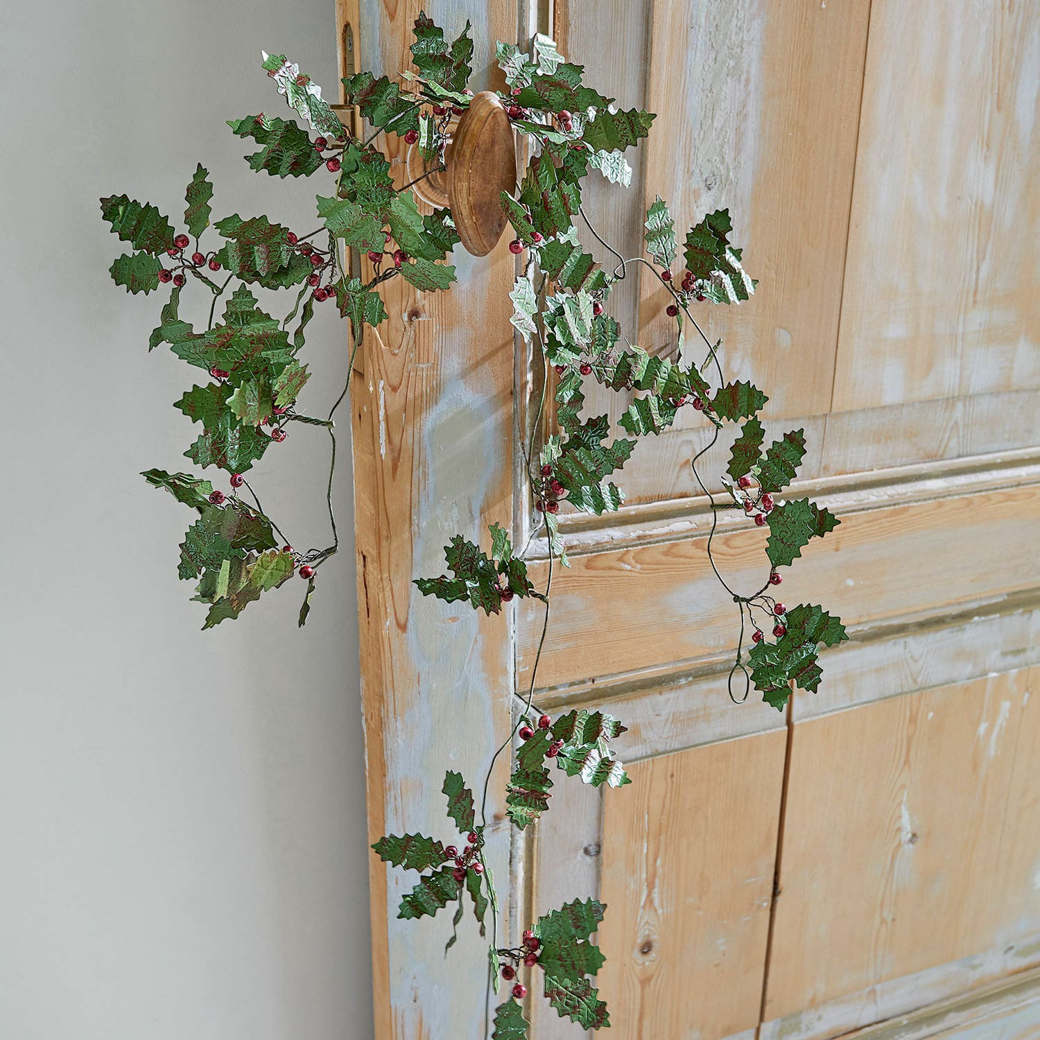 Guirlande Fleur Couronne décorative avec feuilles vertes et baies rouges accrochée à une porte en bois, décoration festive