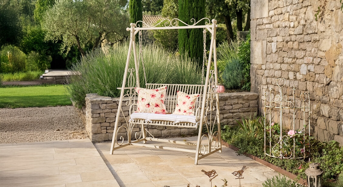 Balançoire de jardin en métal blanc avec coussins rouges et blancs à motifs floraux sur terrasse en pierre
