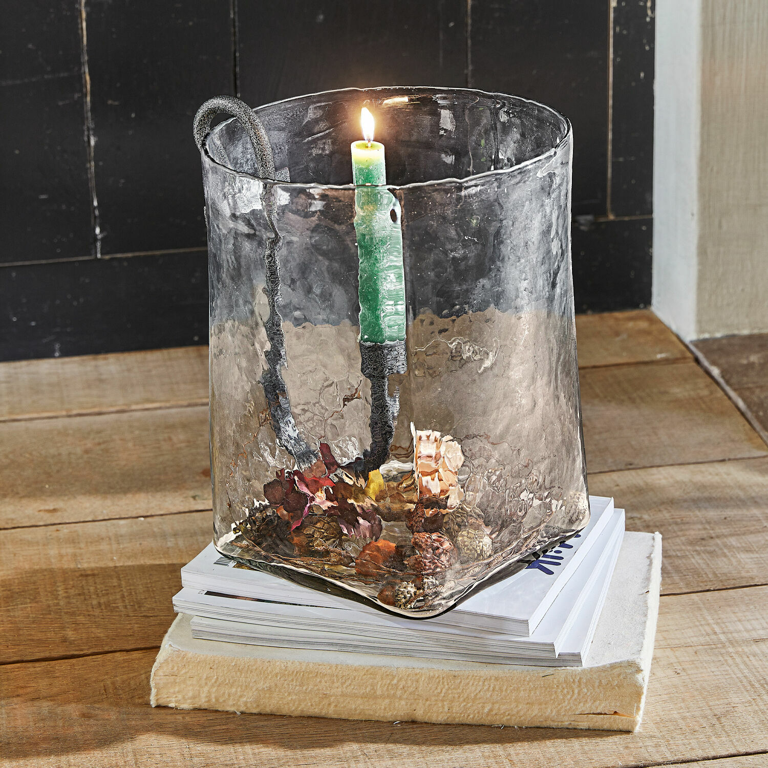 Windlicht Arcene Glazen kandelaar met metalen handvat en groene kaars op houten tafel met dennenappeldecoratie