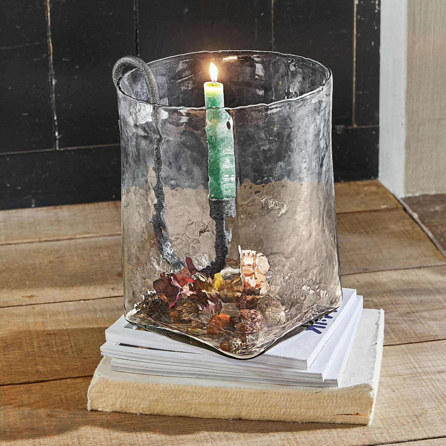 Windlicht Arcene Glazen kandelaar met metalen handvat en groene kaars op houten tafel met dennenappeldecoratie