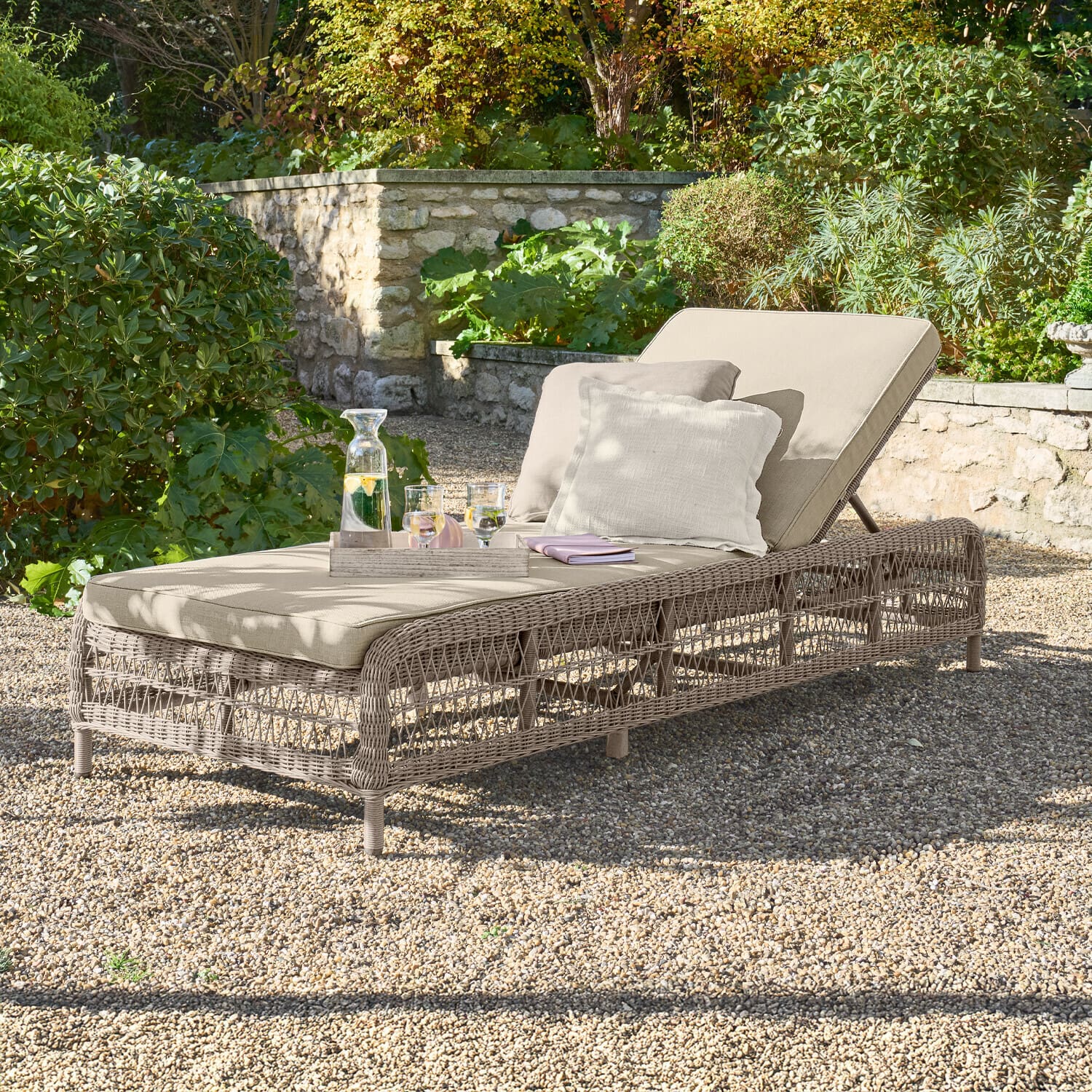 Ligstoel Hereford Tuinligstoel met beige kussen en gevlochten frame op grind in groene tuin