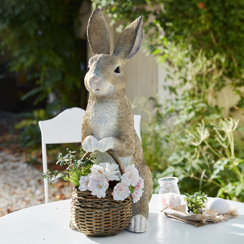 Decoratief konijn van kunststof in natuurlijke kleur met rieten mand en bloemen op tuintafel