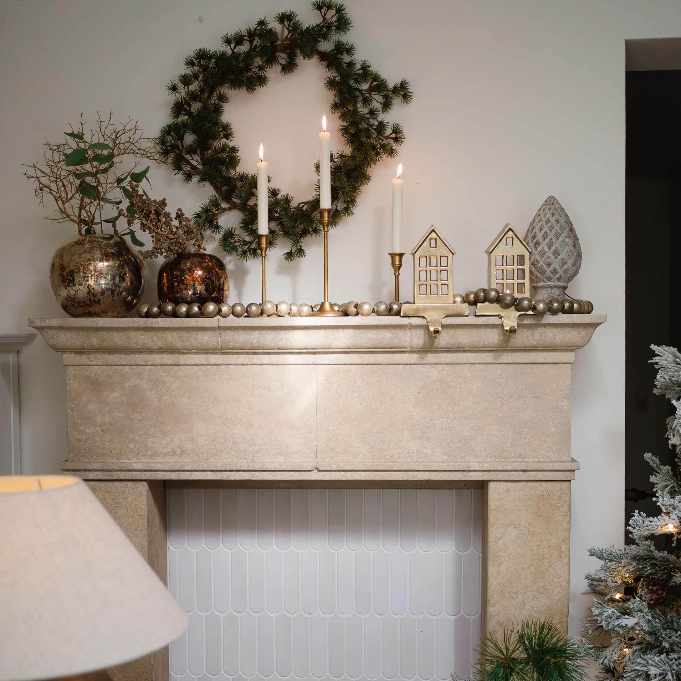 Cheminée en pierre beige décorée d'une couronne verte, bougeoirs dorés et décorations de Noël élégantes