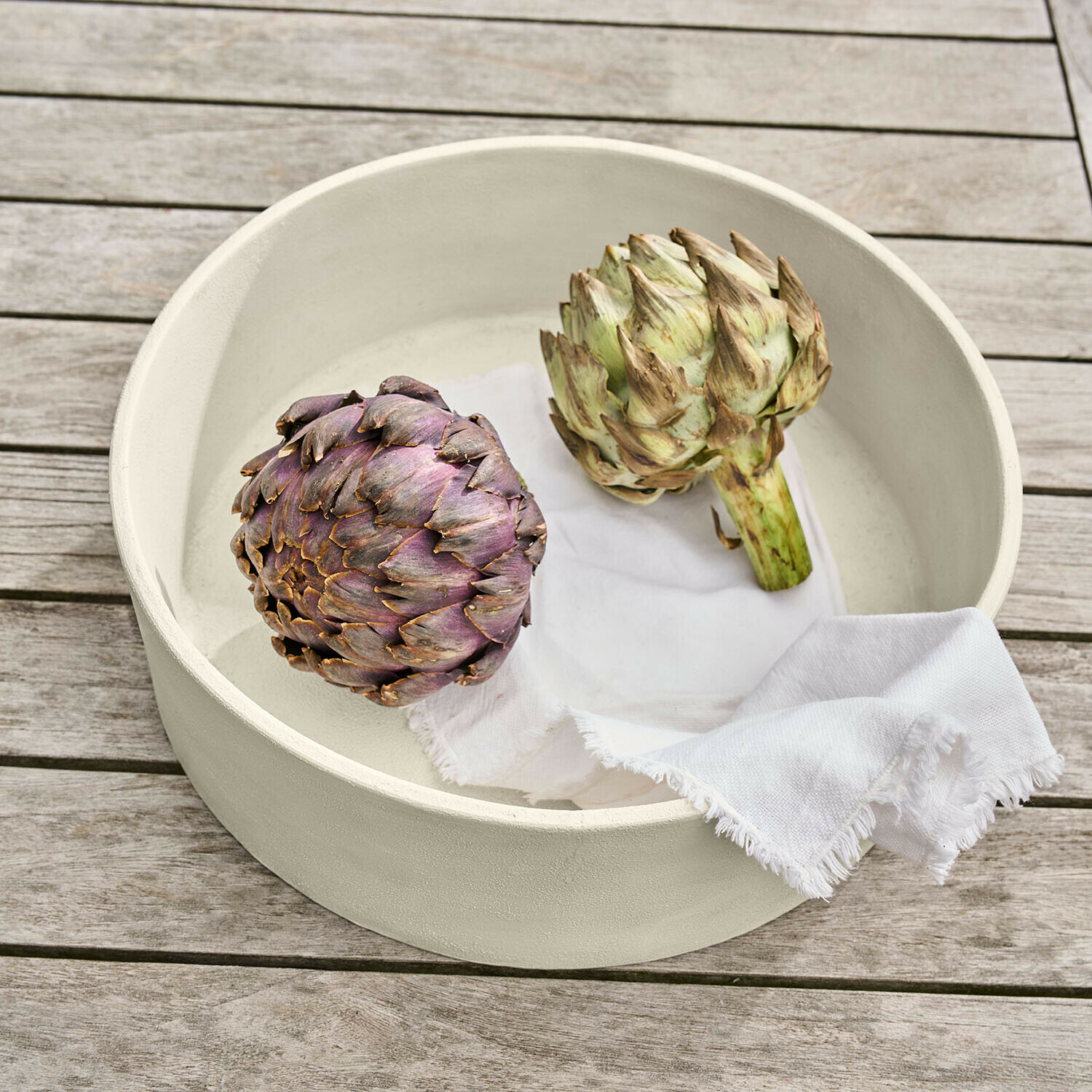 Schaal Islene Ronde crème keramische schaal met twee artisjokken en een wit doek op een houten tafel