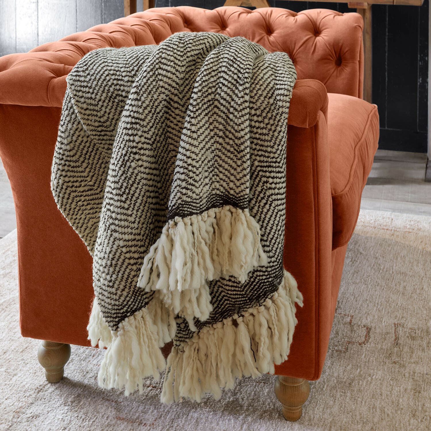 Plaid doux à franges noir et blanc posé sur un canapé en velours orange dans un salon moderne