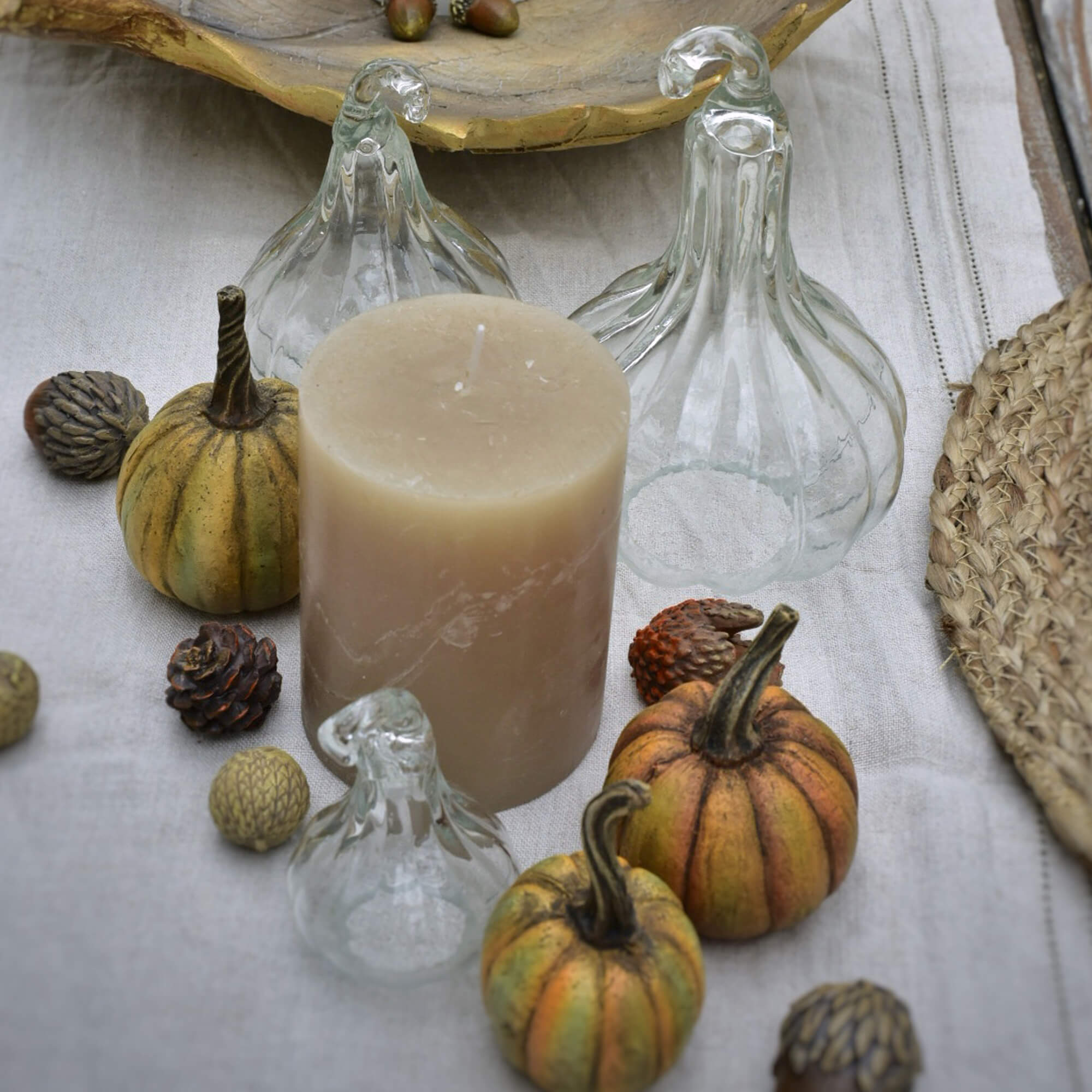 Beige kaars met decoratieve glazen pompoenen en kleine herfstversieringen op linnen doek